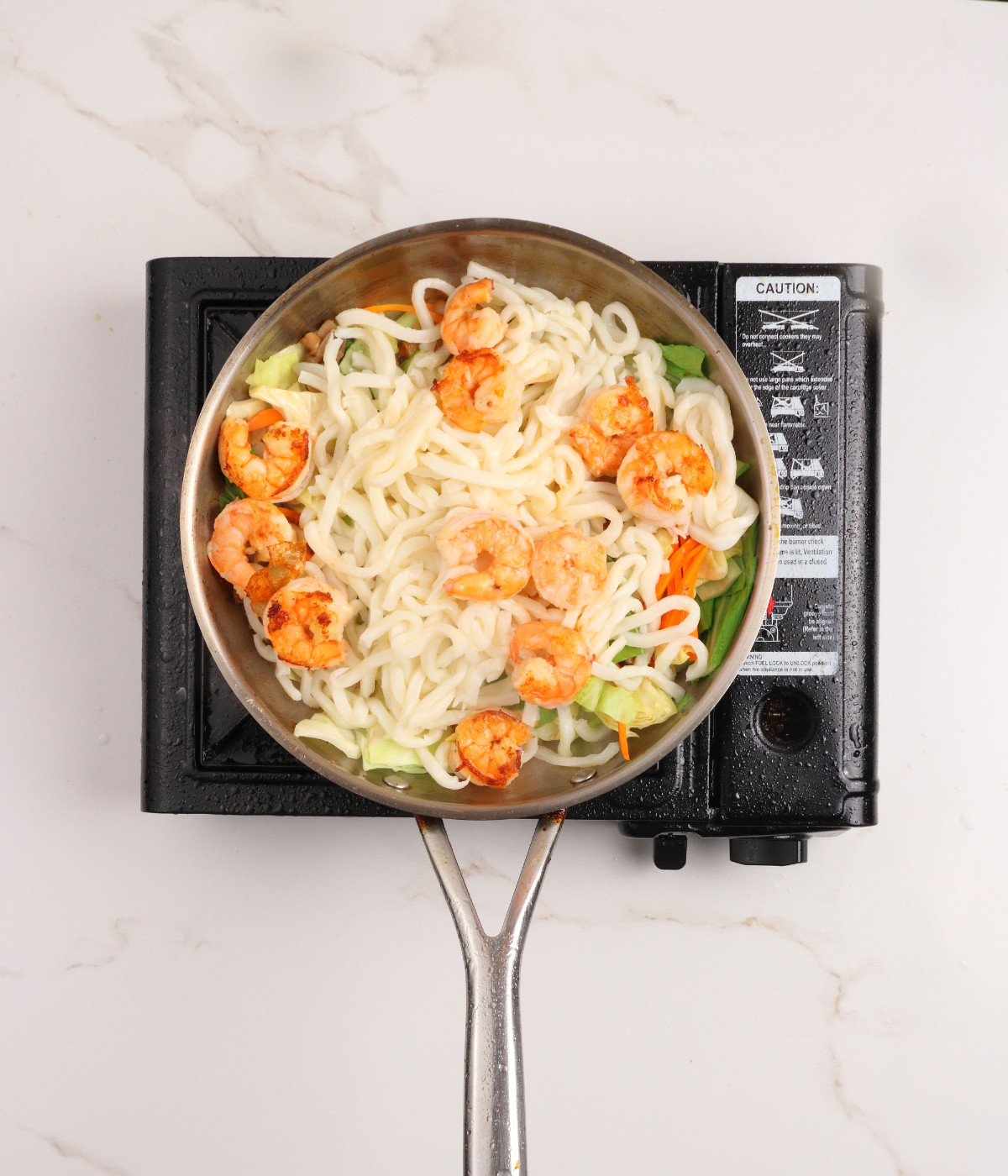 Udon, shrimp, mushrooms, carrots, cabbage and pak choi cooking in a pan.