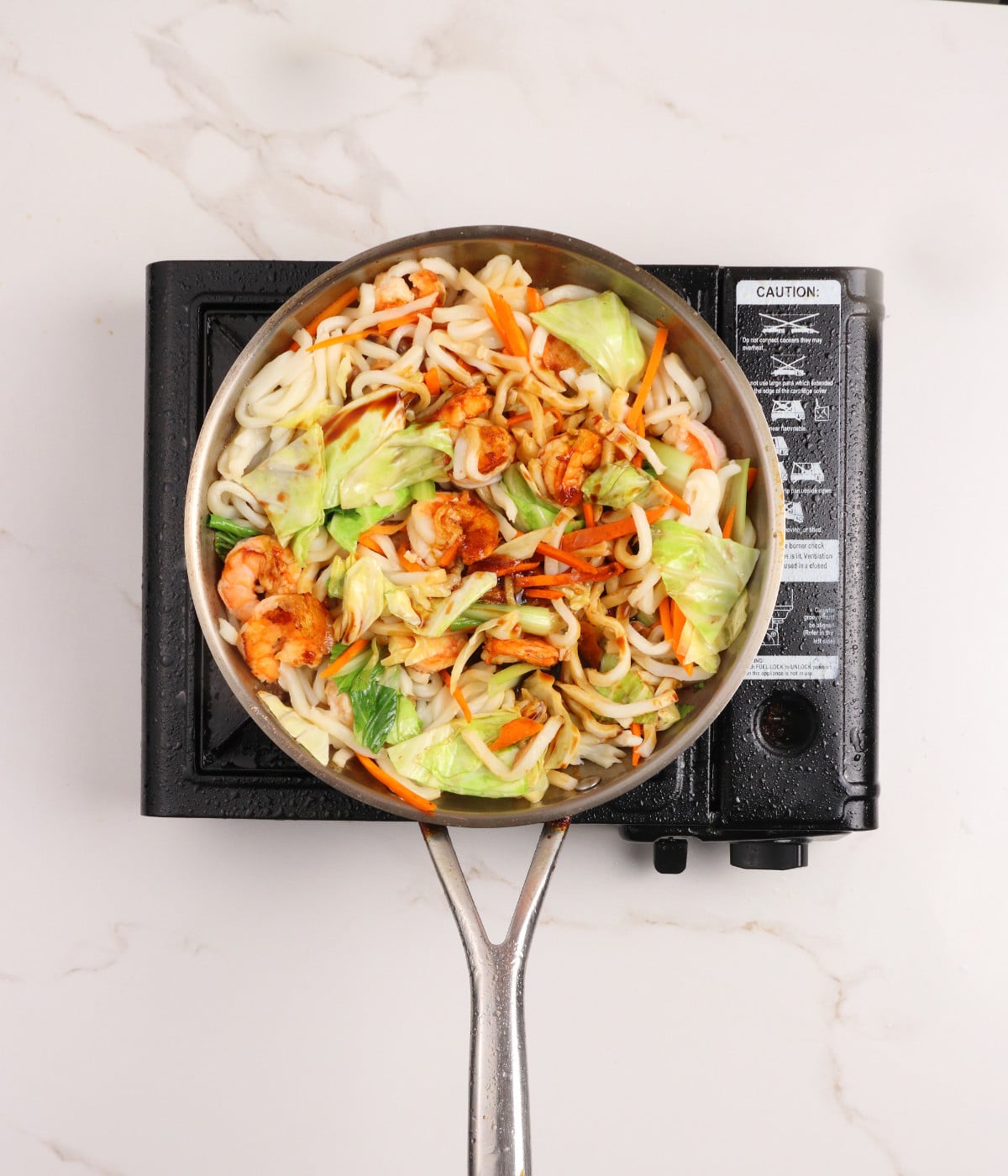 Udon, shrimp, mushrooms, carrots, cabbage, soy marinade and pak choi cooking in a pan.