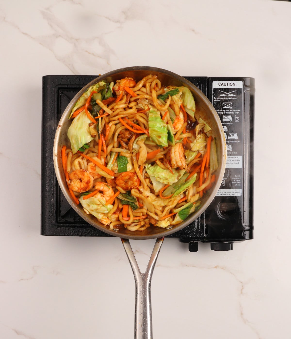 Udon, shrimp, mushrooms, carrots, cabbage, soy marinade and pak choi tossed in a pan.