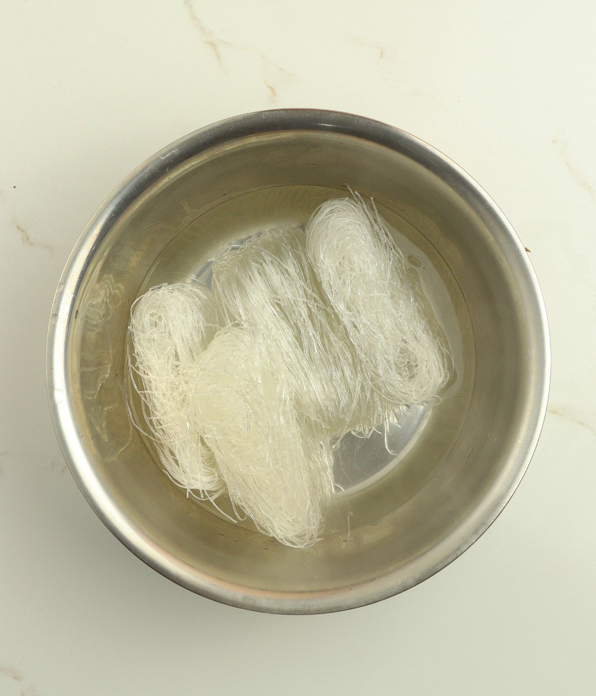 Vermecelli noodles and water in a silver bowl.