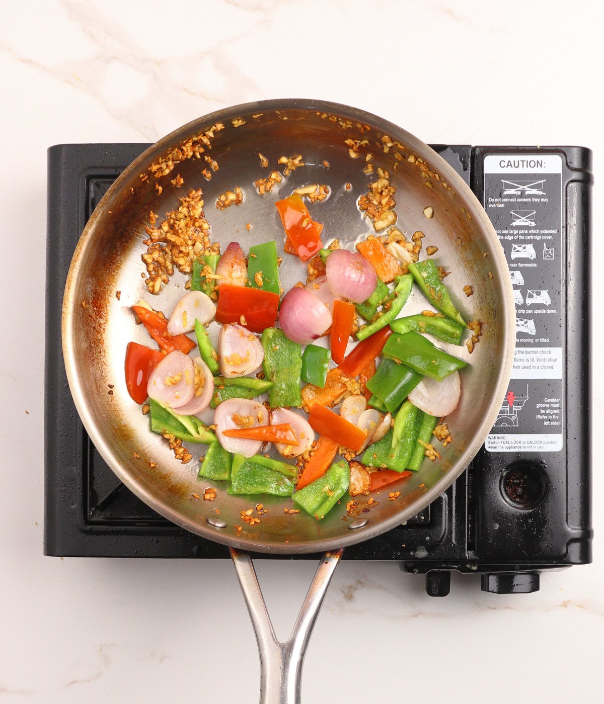 Garlic, ginger, red, green capsicum peppers and red onions in a pan.