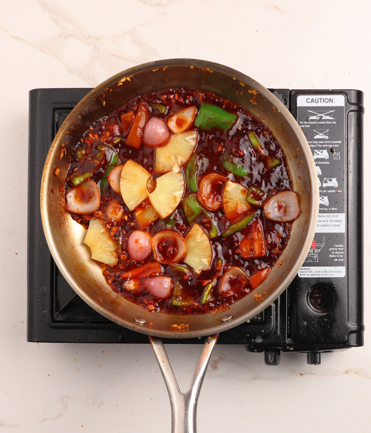 Garlic, ginger, red, green capsicum peppers, pineapples, sweet sauce and red onions in a pan.