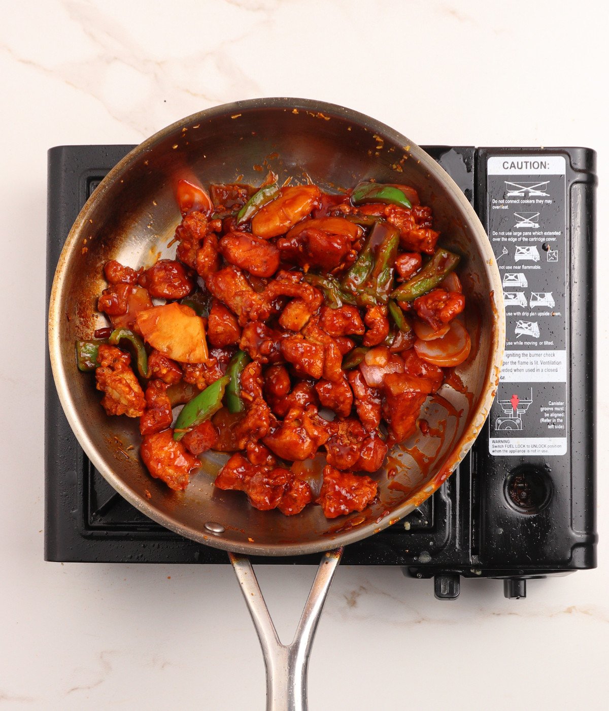 Red, green capsicum peppers, pineapples, crispy chicken and sweet and sour sauce in a pan.