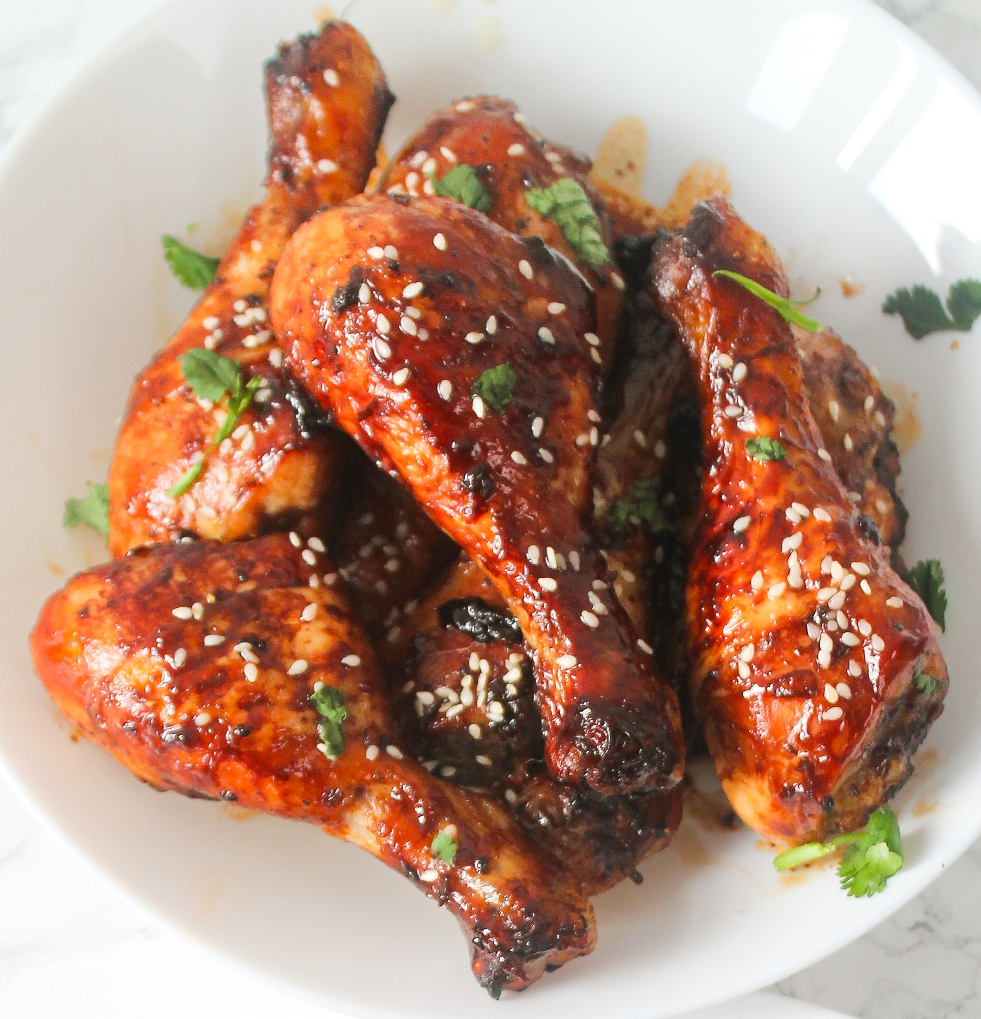 Sticky honey soy drumsticks on a white plate tapped with sesame seeds and parsley.