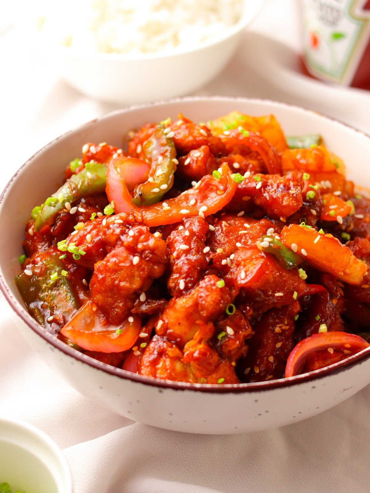 Sweet and sour chicken in a bowl topped with seeds and scallions.