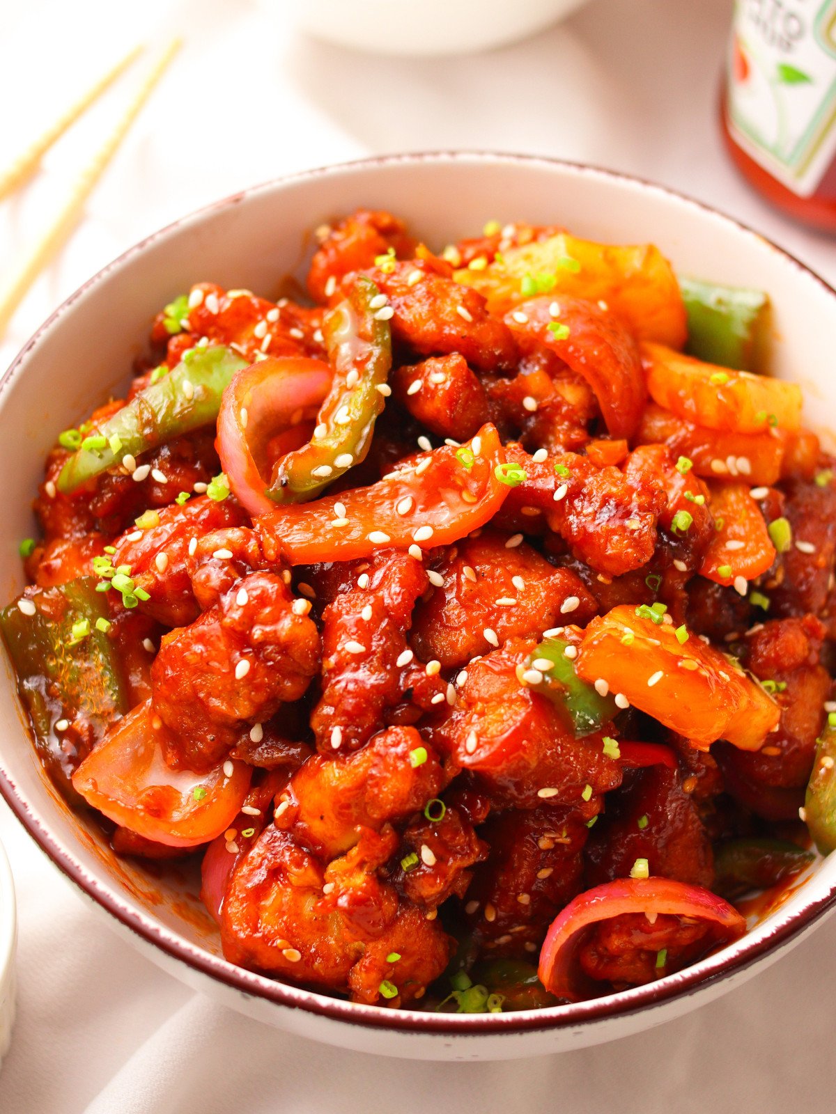 Sweet and sour chicken in a bowl topped with sesame seeds and scallions.