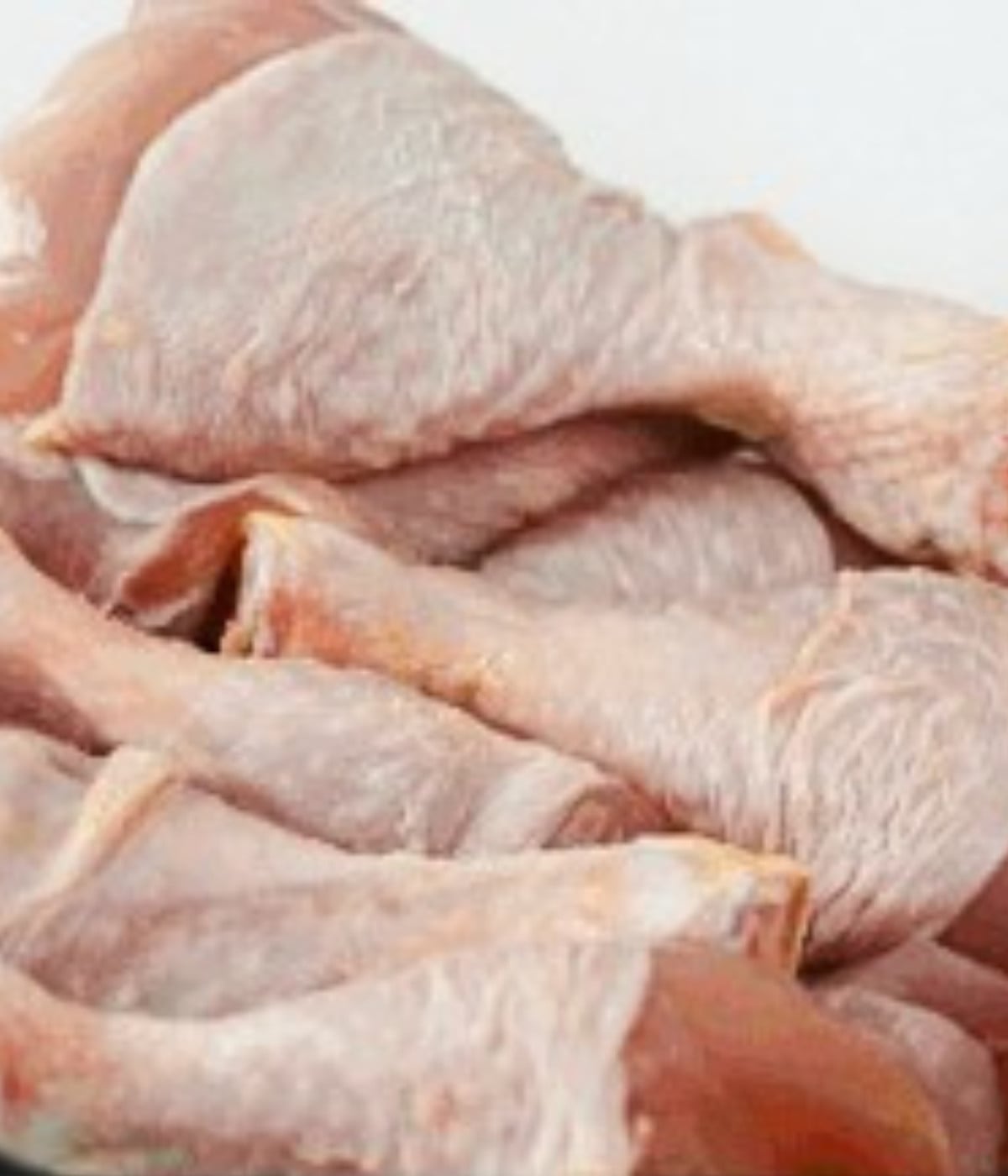 Uncooked drumsticks in a white bowl.