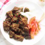 Beef chunks on a white plate with tomatoes, onions and toothpicks.