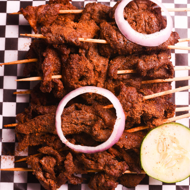 Beef suya on kebab sticks with red onions and cucumber.