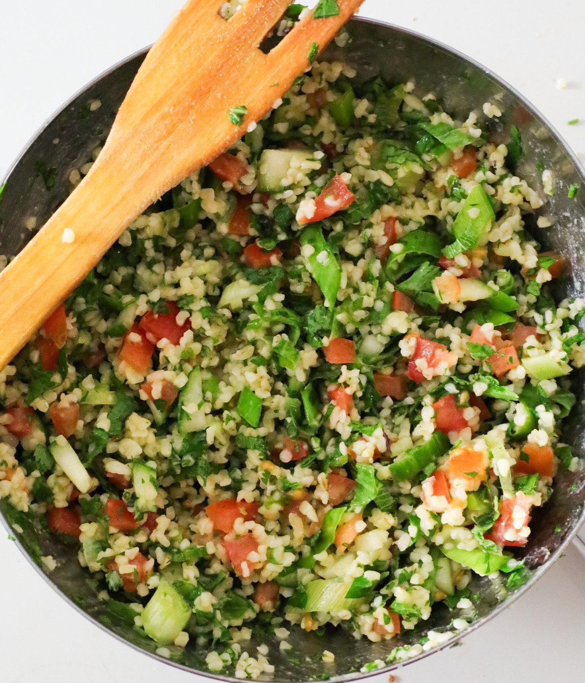 Fresh chopped herbs, scallions, tomatoes, bulgur wheat dressing and cucumbers tossed in a bowl.