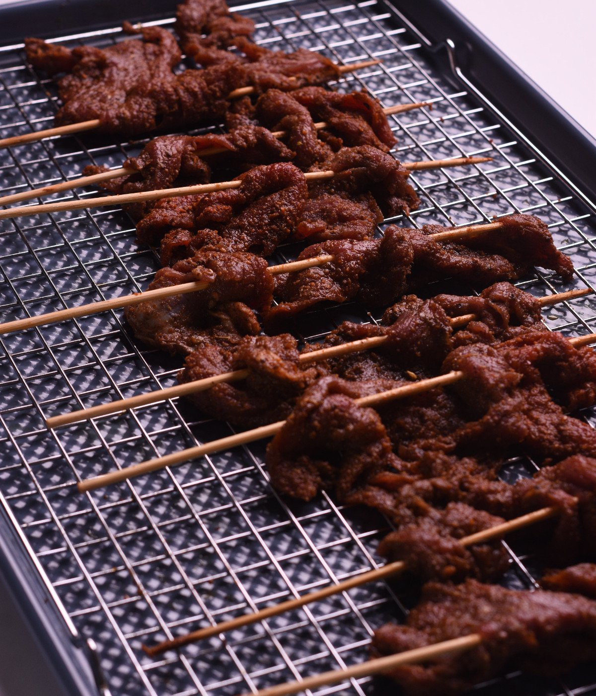 Grilled flank steak on kebab sticks on a baking tray.