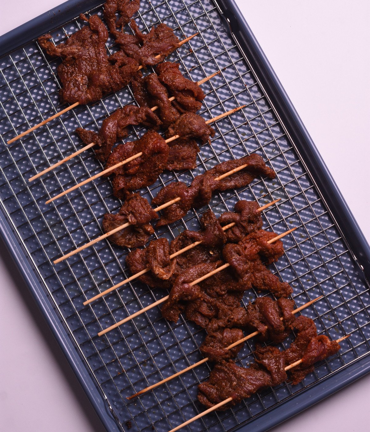 Half marinated flank steak on kebab sticks on a baking tray.