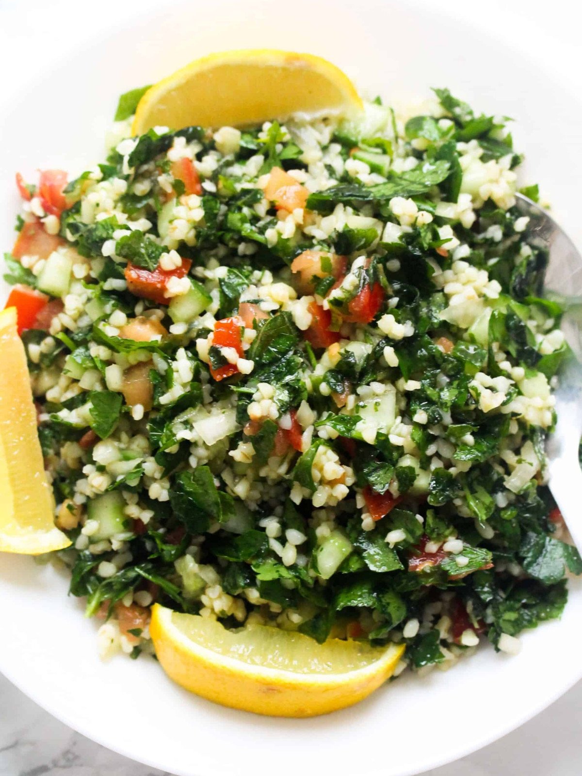 Lebanese style Tabbouli salad in a white plate with lemon wedges and a silver spoon.