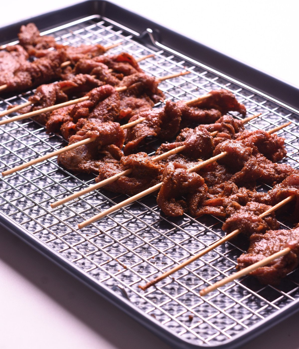 Marinated flank steak on kebab sticks on a baking tray.
