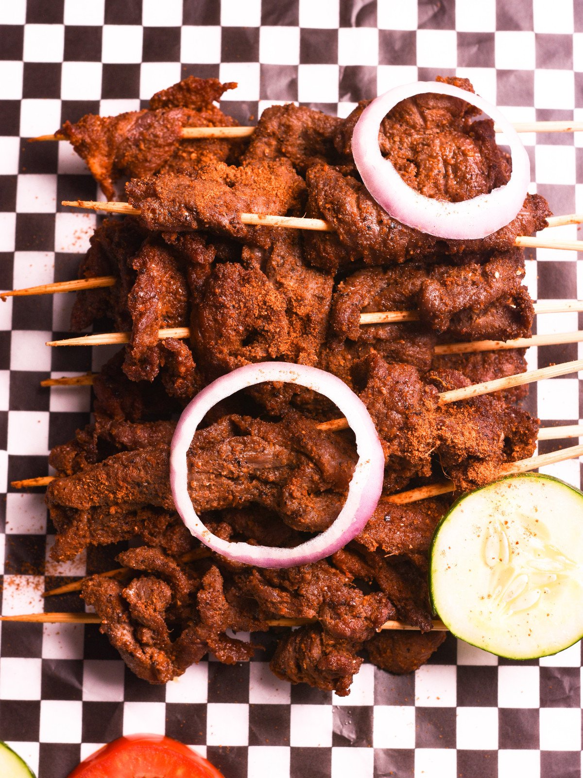 Nigerian beef suya on kebab sticks with red onions, tomato and cucmbers.