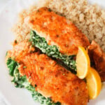 Salmon stuffed with ricotta and spinach and lemon wedges on a bed of quinoa on a white plate.