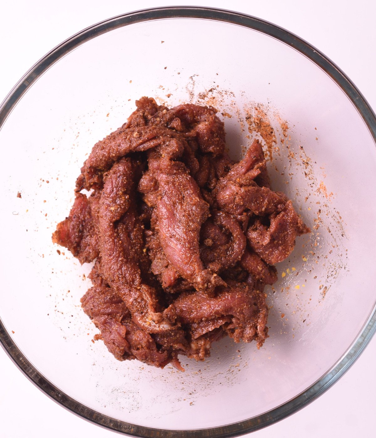 Sliced flank steak marinated with yaji spice and seasoning in a glass bowl.