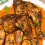 Suya chicken legs served with jollof rice, plantain and fresh parsley on a white plate.