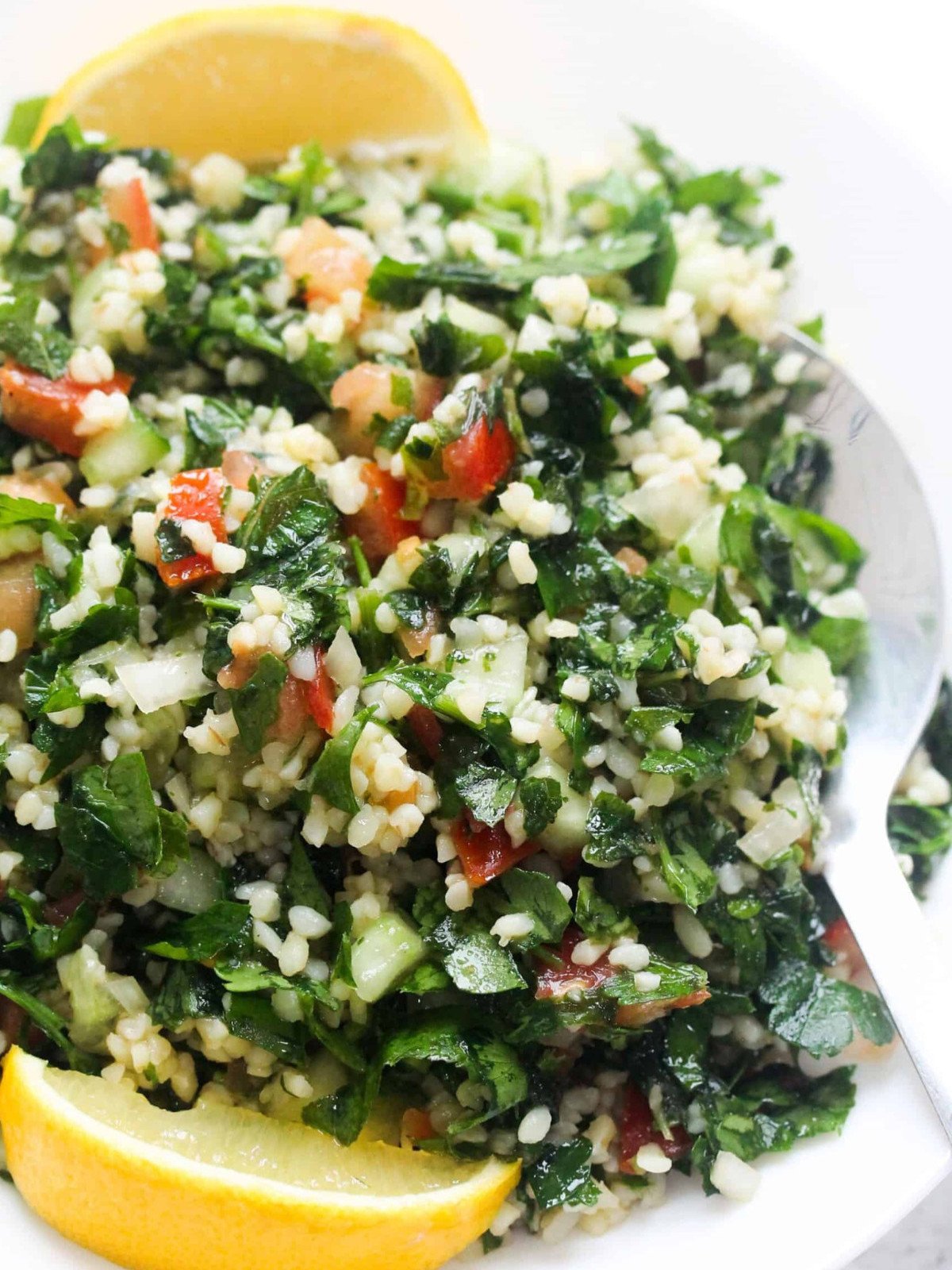Tabbouli salad in a white plate with lemon wedges and a silver spoon.