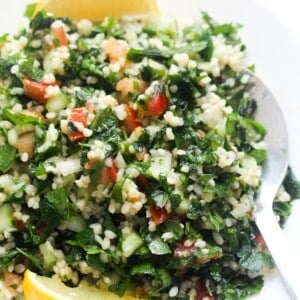 tabbouleh salad on a white plate with two lemon wedges and a silver spoon