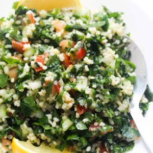 tabbouleh salad on a white plate with two lemon wedges and a silver spoon