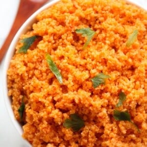 tomato couscous garnished with parsley served in a white bowl with a brown spoon on the table