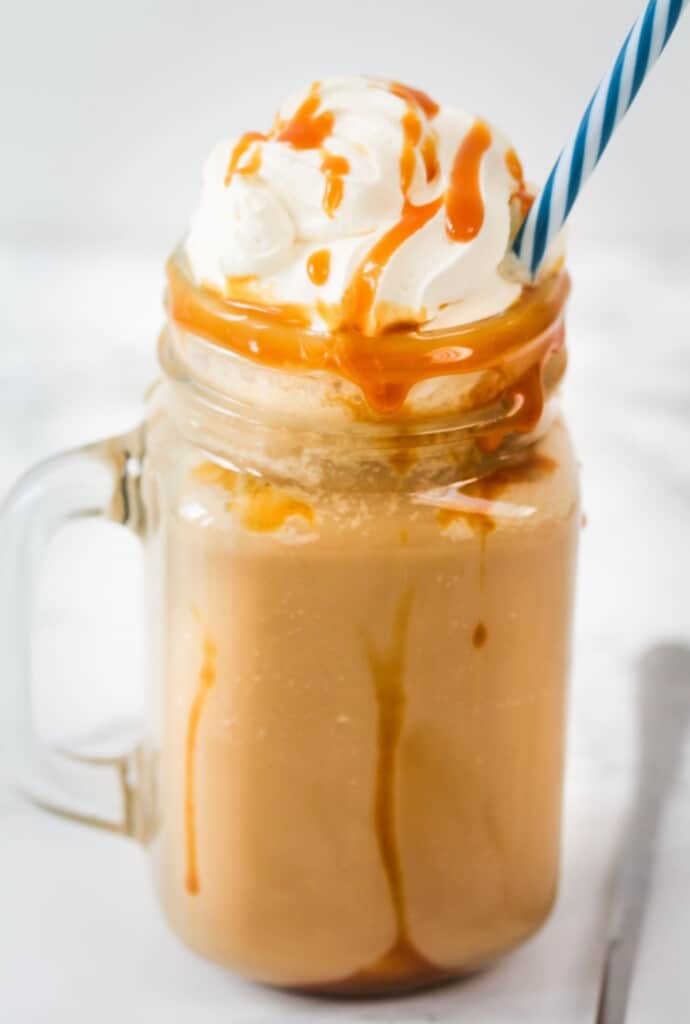 caramel Frappuccino with whipped cream and caramel sauce in a jar with a blue straw