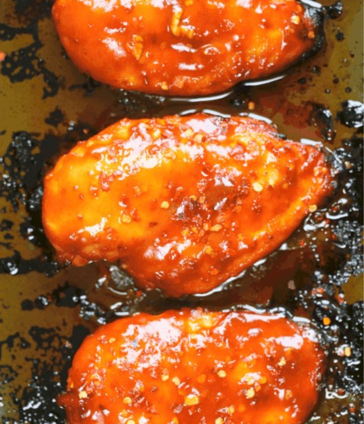 Baked siraccha chicken breasts on a baking tray.