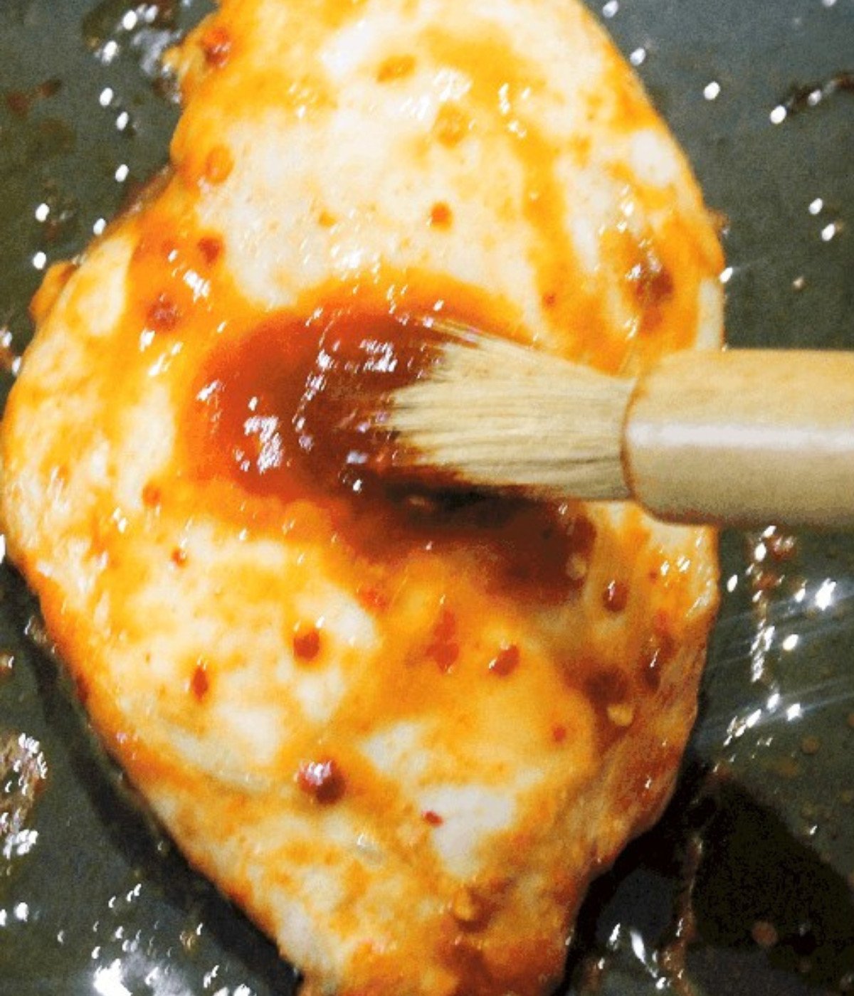 Chicken breast basted with siraccha on a baking tray.