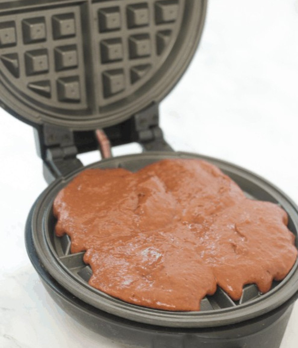 Chocolate waffle batter in a black waffle maker.