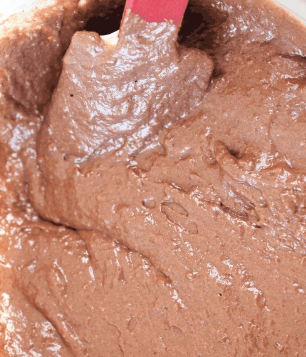 Cocoa powder, flour, milk and eggs mixed in a bowl with a spatula.