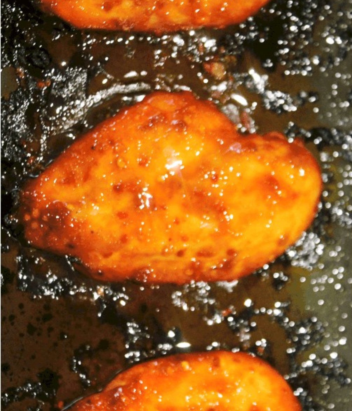 Half cooked siraccha chicken breasts on a baking tray.