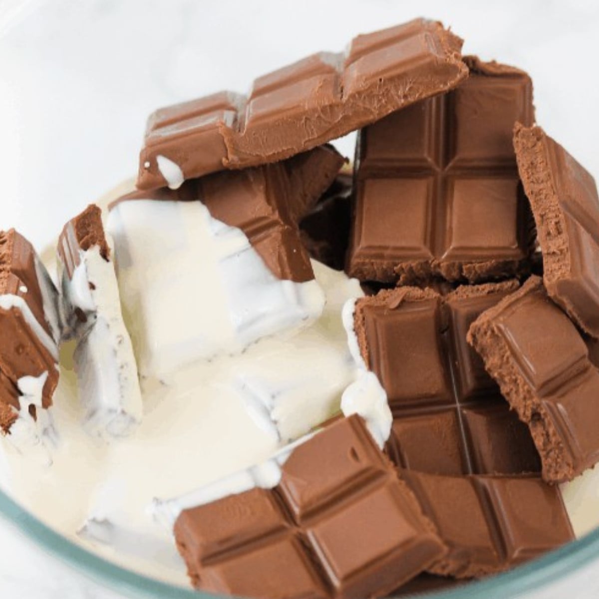 Milk chocolate bars and heavy cream in a glass bowl.