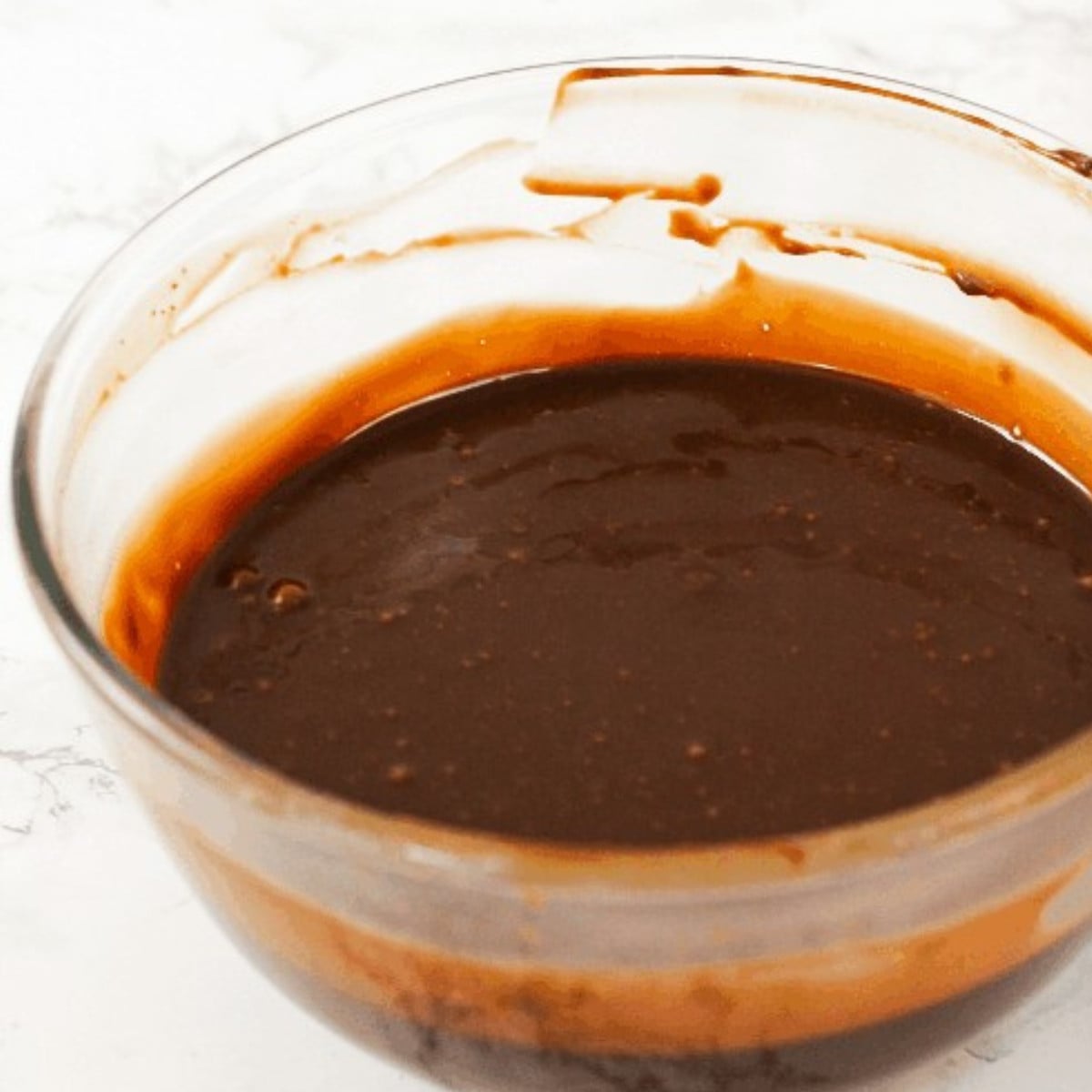 Milk chocolate and heavy cream melted and mixed in a glass bowl.