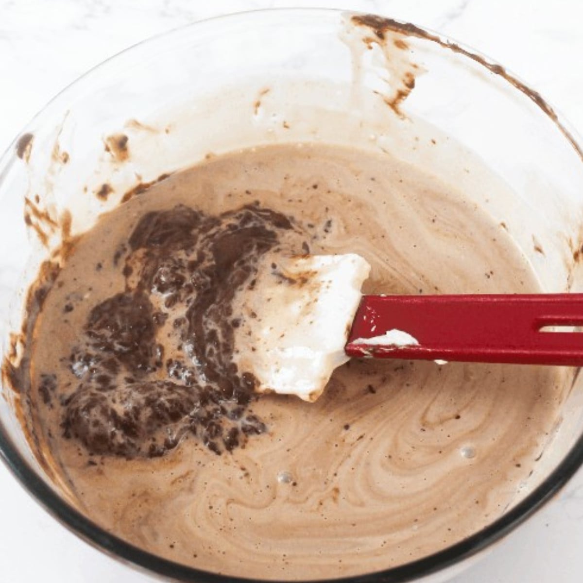 Milk chocolate and heavy cream melted in a glass bowl and a spatula.