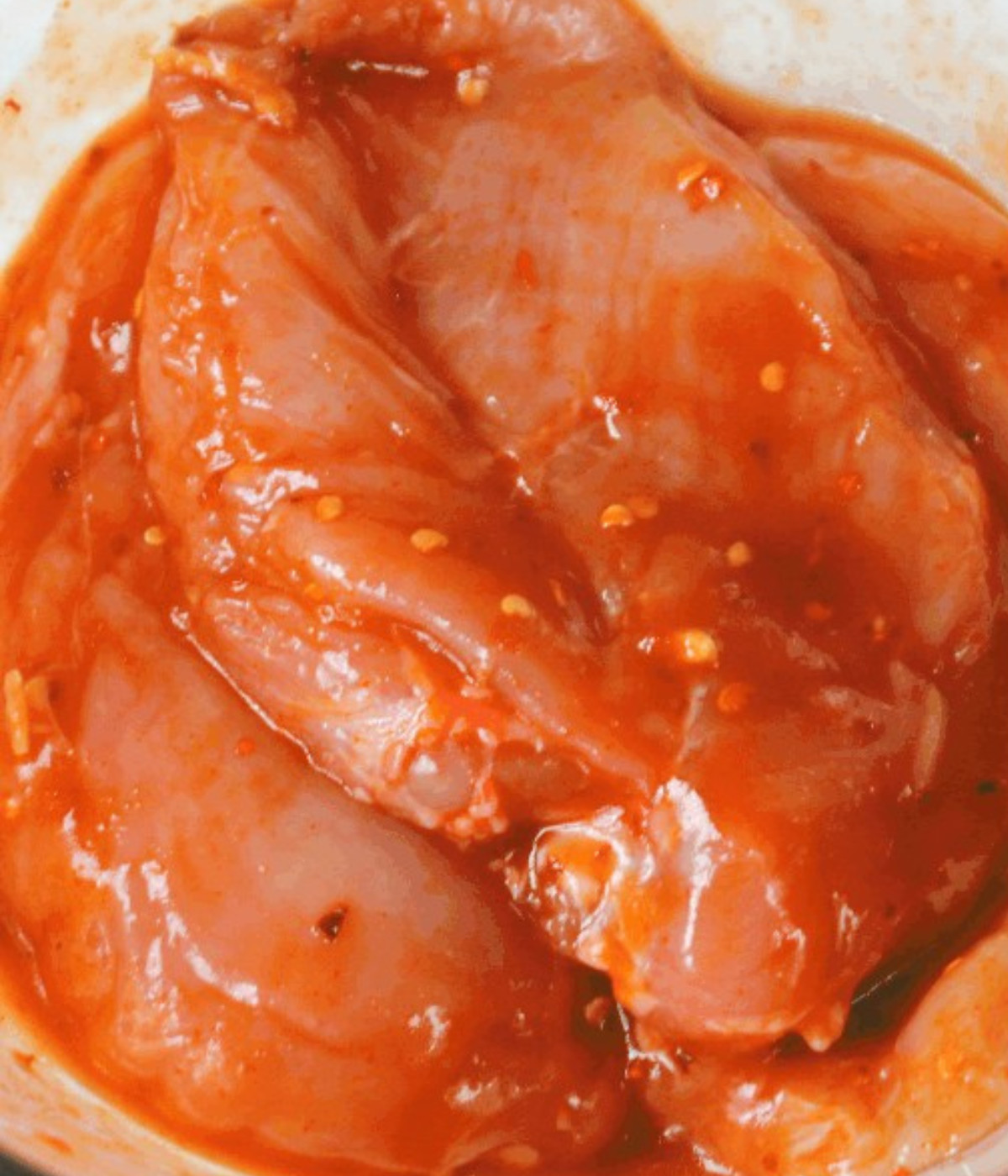 Siraccha marinated chicken breasts in a bowl.