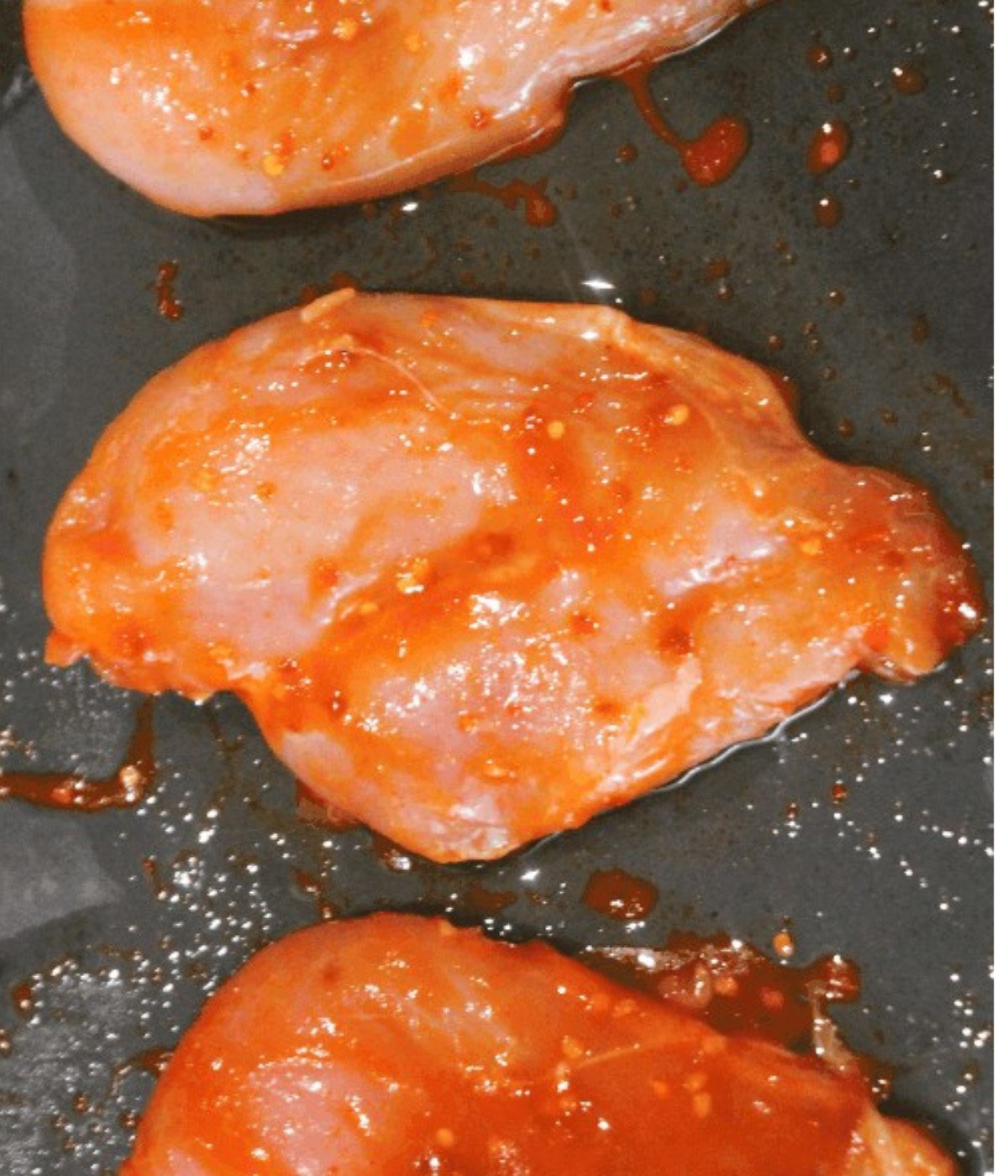 Siraccha marinated chicken breasts on a baking tray.