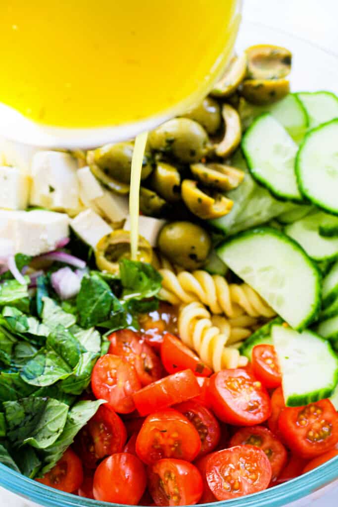 lemon dressing poured into Mediterranean pasta salad