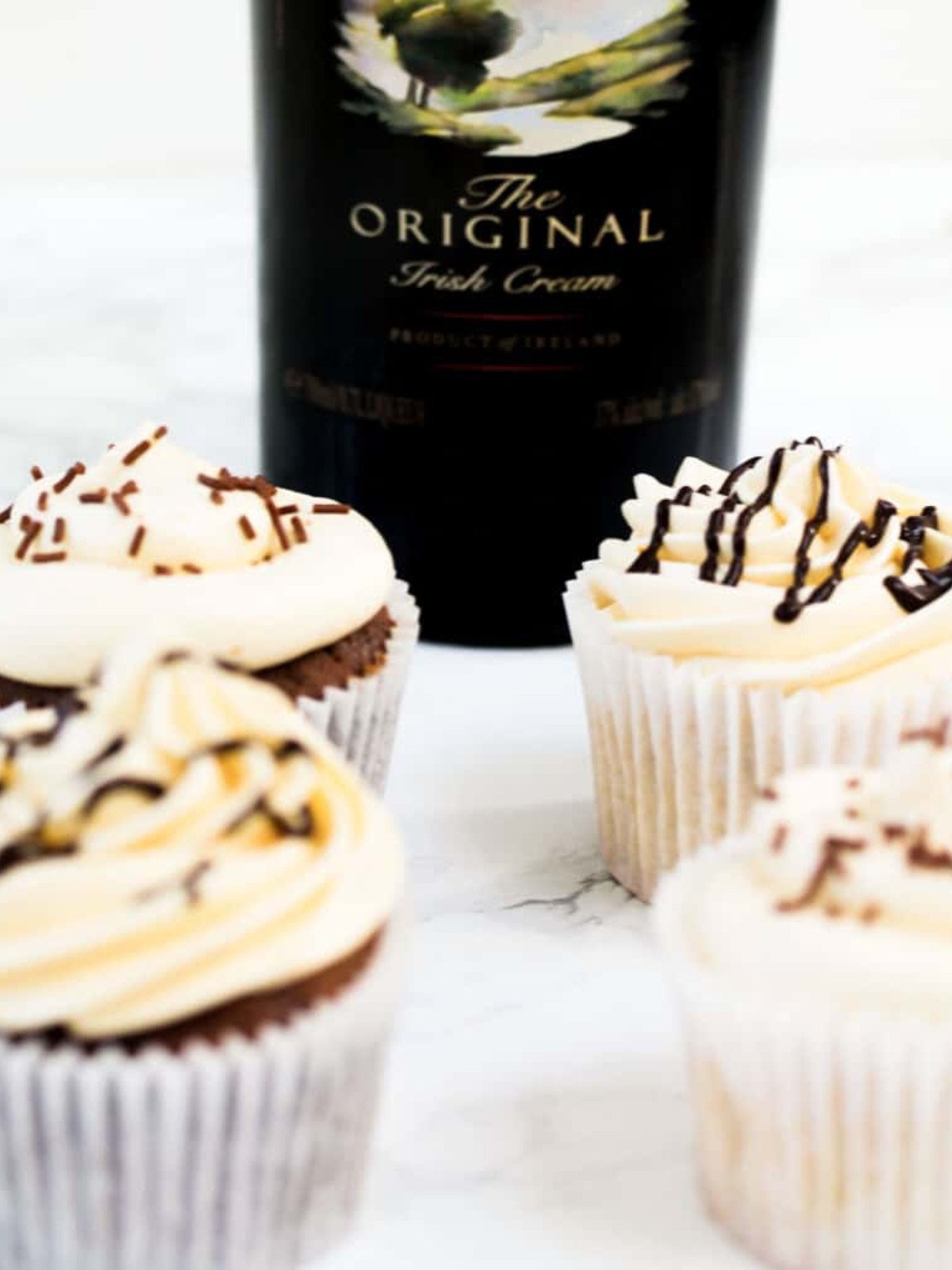 Irish cream cupcakes on a marble table with a bottle of irish cream.