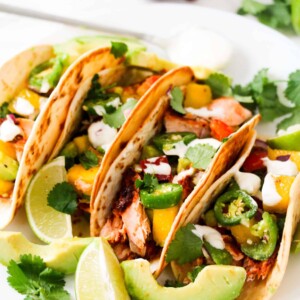 salmon tacos served with lime wedges, avocado and sour cream on a plate