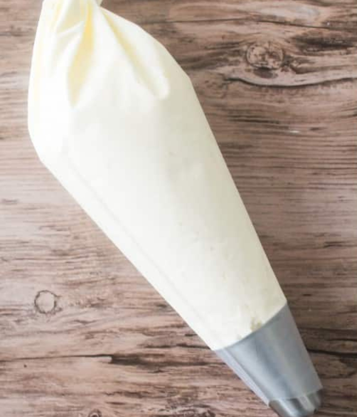 Coconut buttercream in a piping bag on a wooden table.