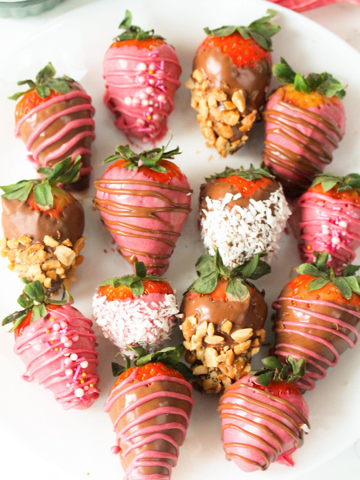 Chocolate covered straberries with nuts and coconut on a white plate.