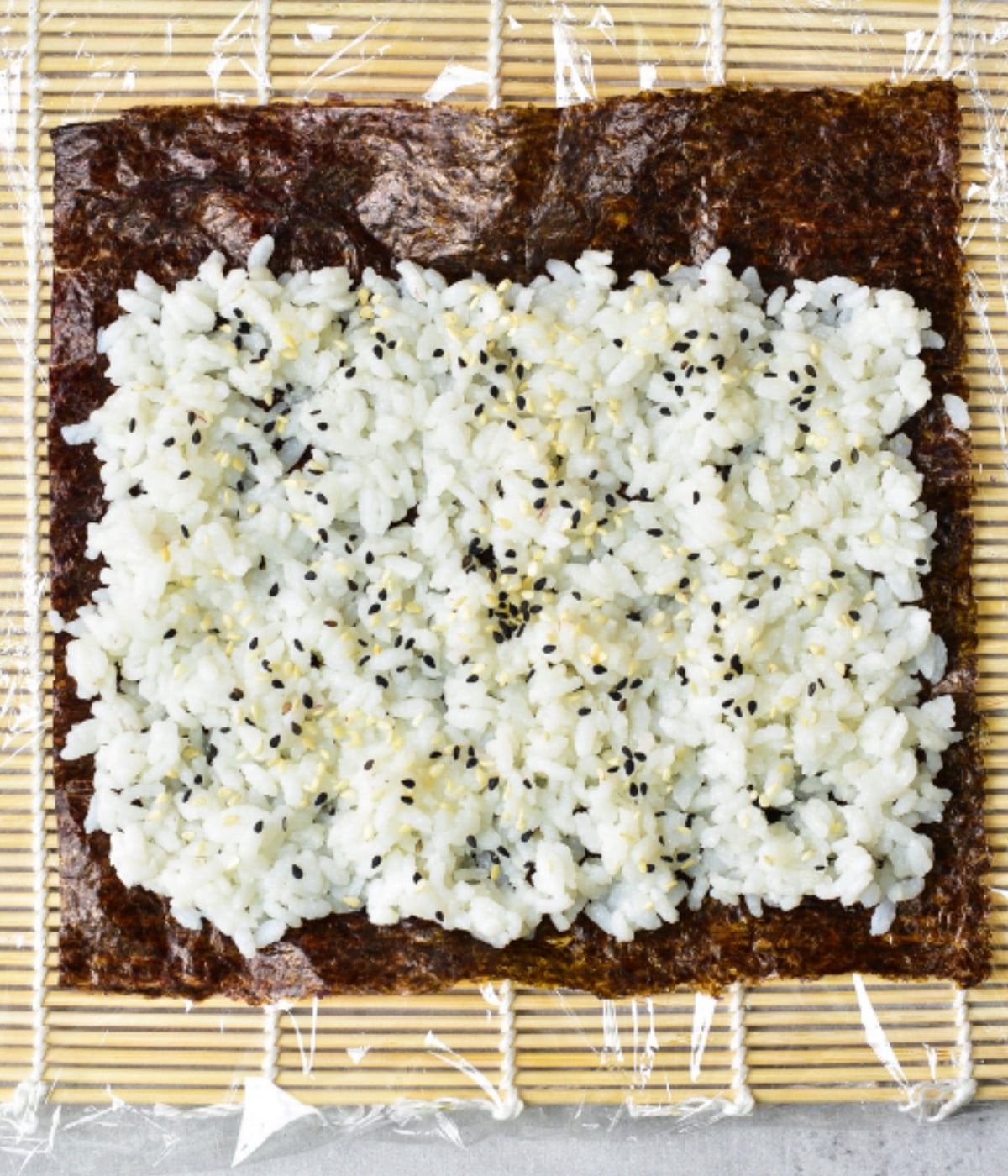 A matt with seaweed, white rice and sesame seeds on top.
