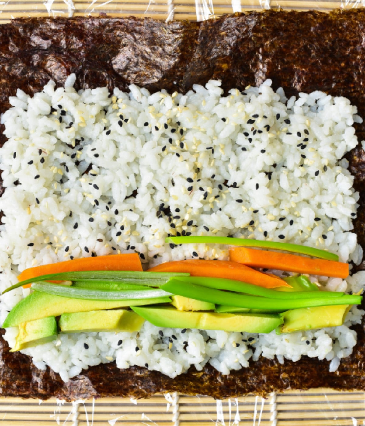 A matt with seaweed, white rice and sesame seeds, sweet potato and avocado on top.