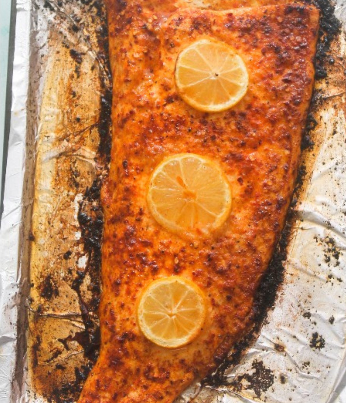 Baked Salmon fillet on a baking tray lined with foil with three lemon slices on top.