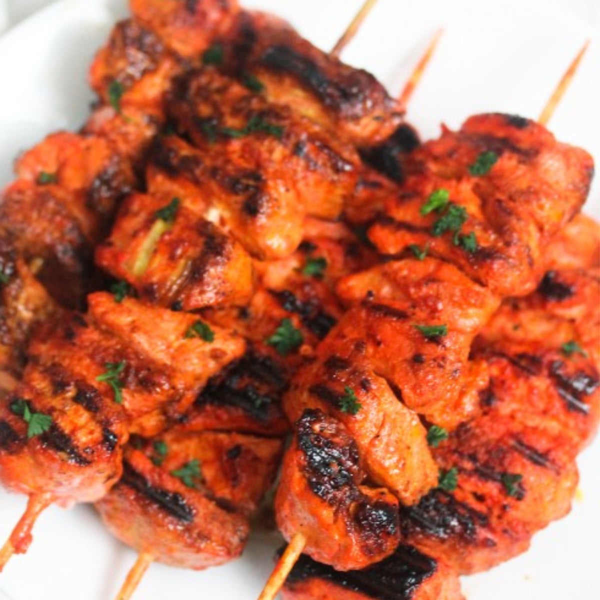 Cooked tandoor chicken skewers topped with herbs on a white plate.
