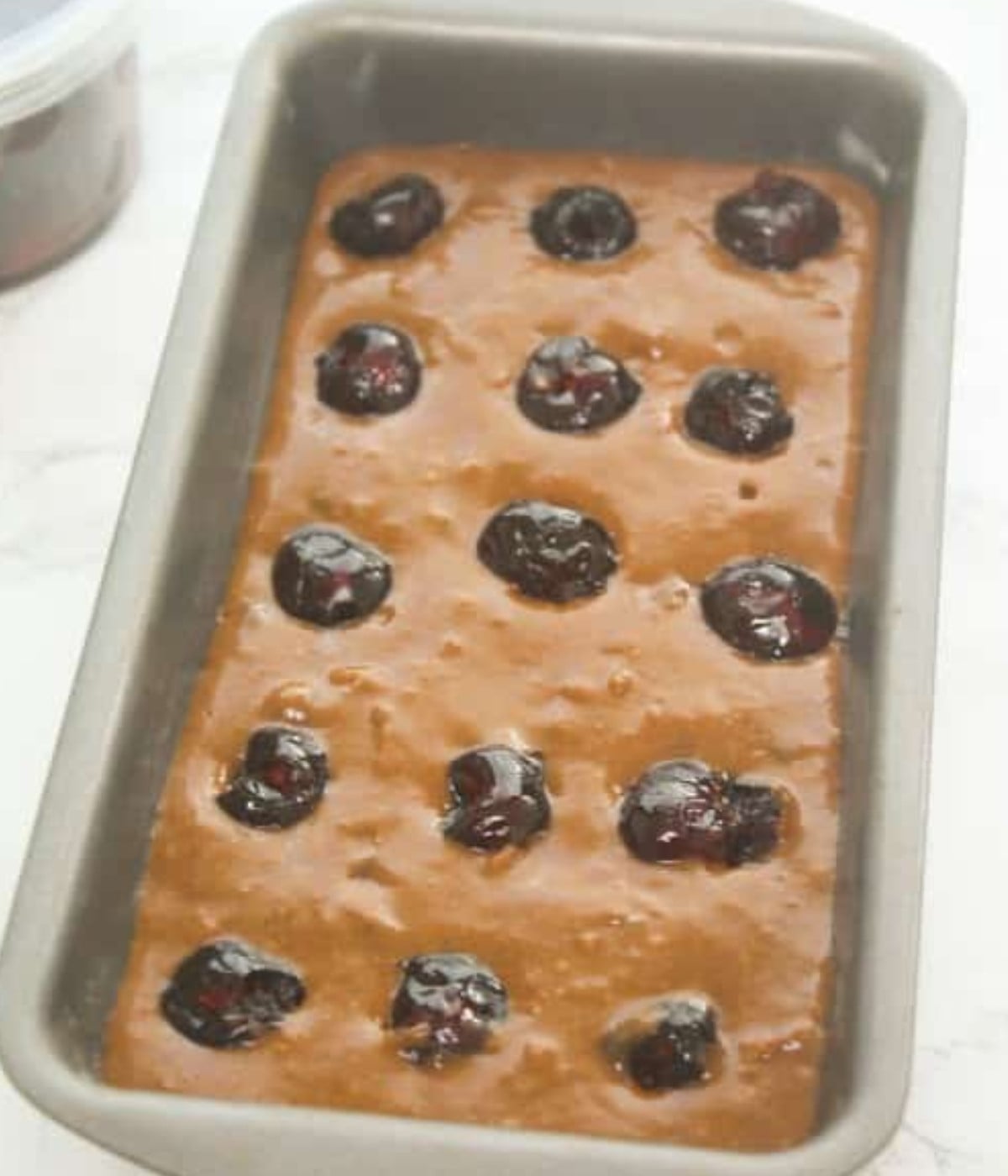 Jamaican buns batter with cherries on top in a loaf tin.