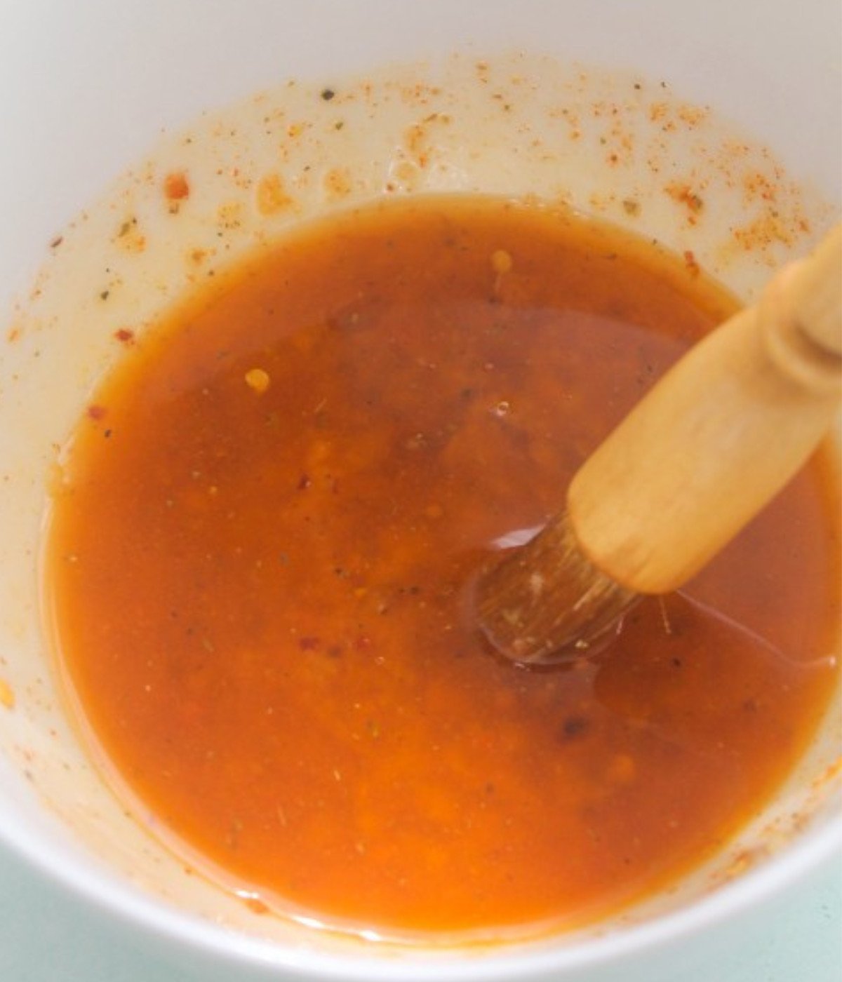 Lemon juice, oil, pepper, haerbs and garlic mixed in a white bowl.