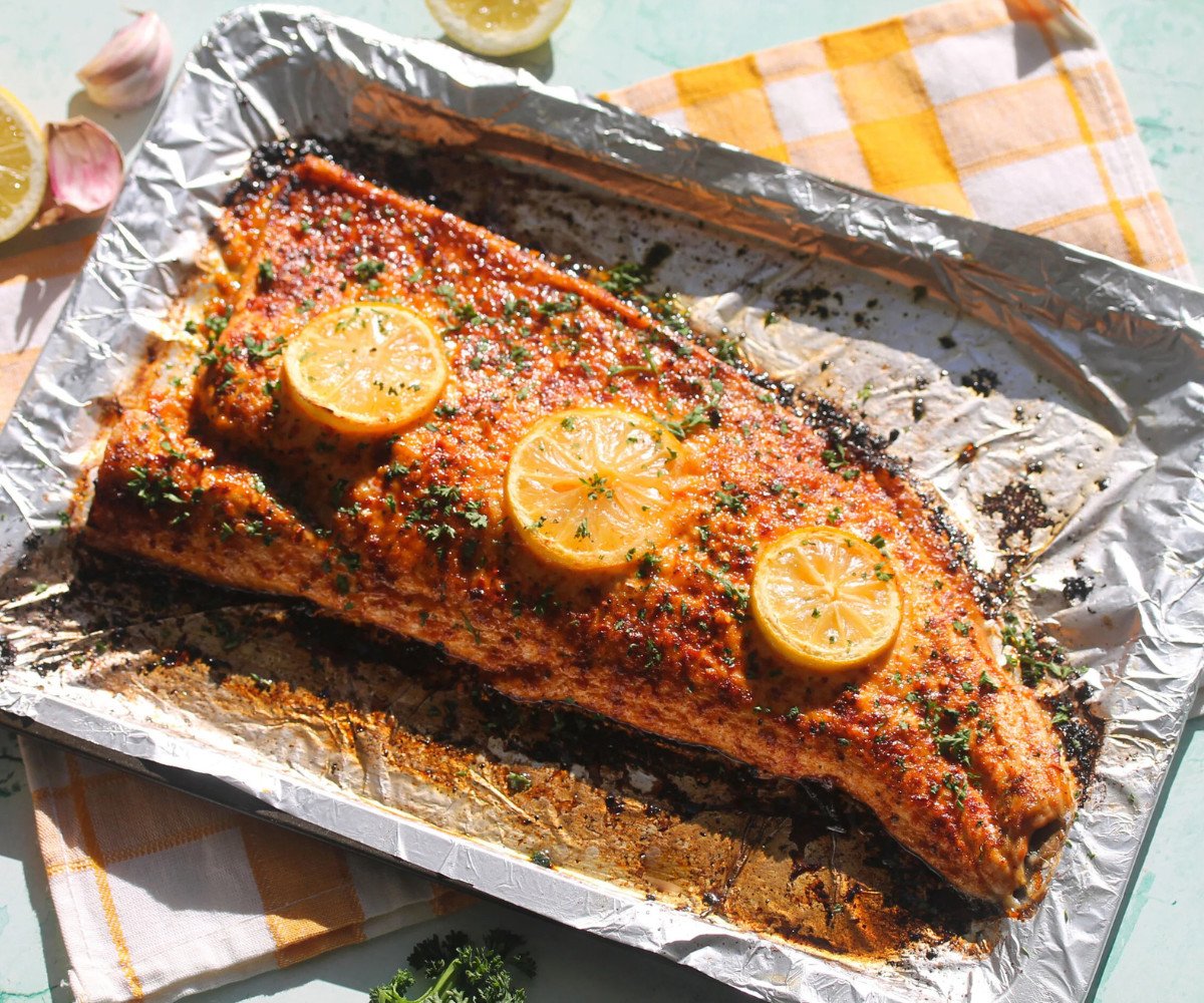Lemon pepper salmon on a lined baking tray garnished with fresh herbs.