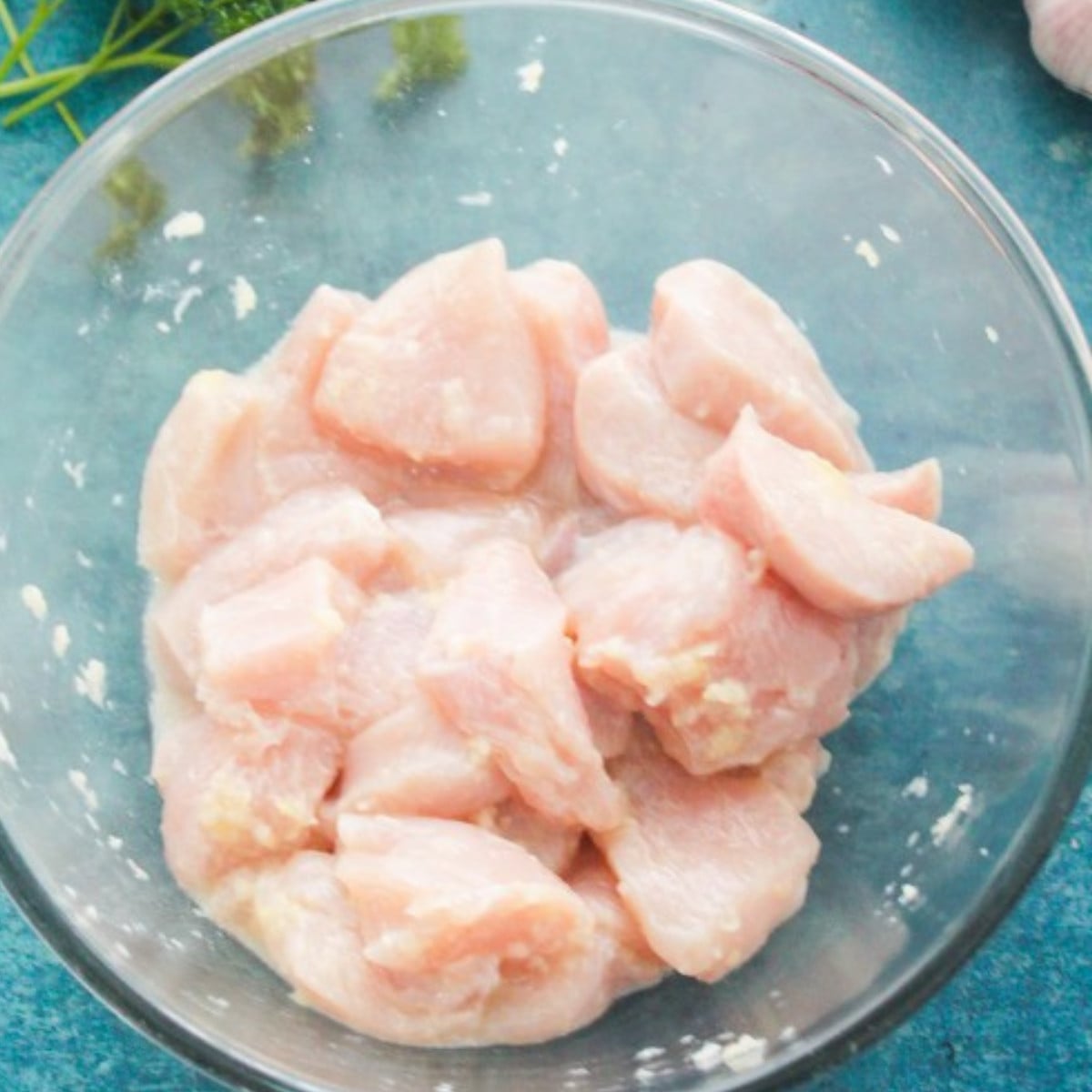 Marinated chicken chopped in cubes with oil in a glass bowl.